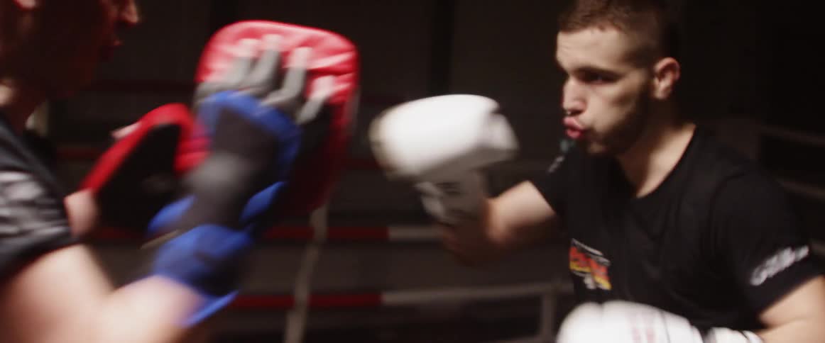 Two men fight each other in a boxing ring with bright strobe lights flashing