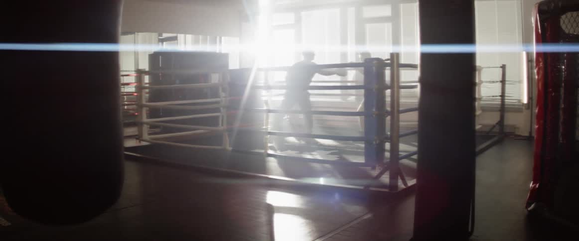 The sun shining through the windows creates a silhouette of two men training in a ring in the gym