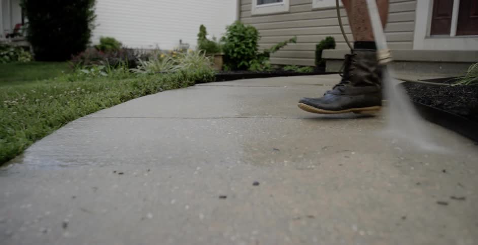A man is power washing a sidewalk