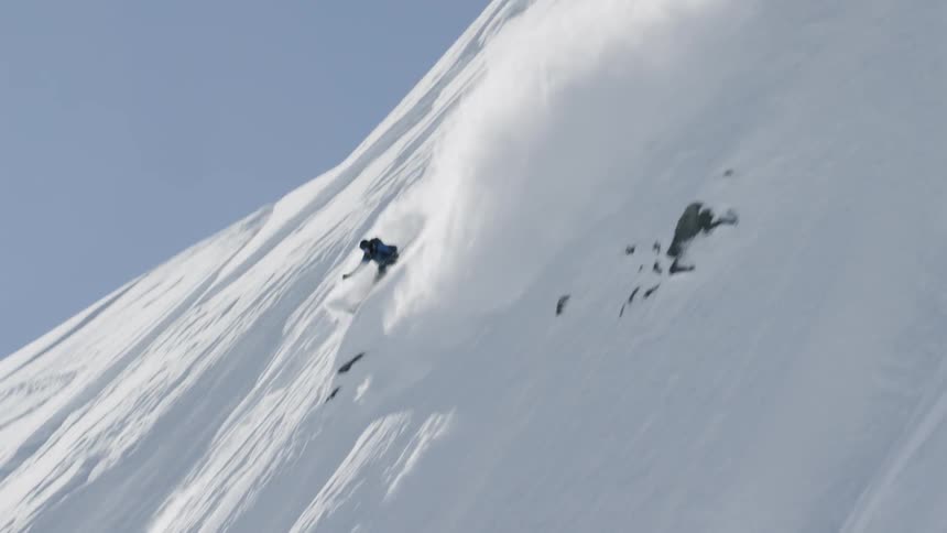 A skier creates a huge plume of snow as they fly down a steep mountain slope