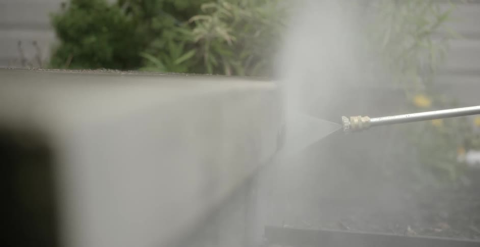 A person uses a power washer on an outdoor wall