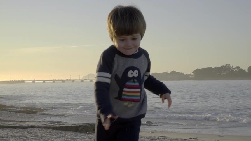 A toddler boy runs and plays on a sandy beach at sunset