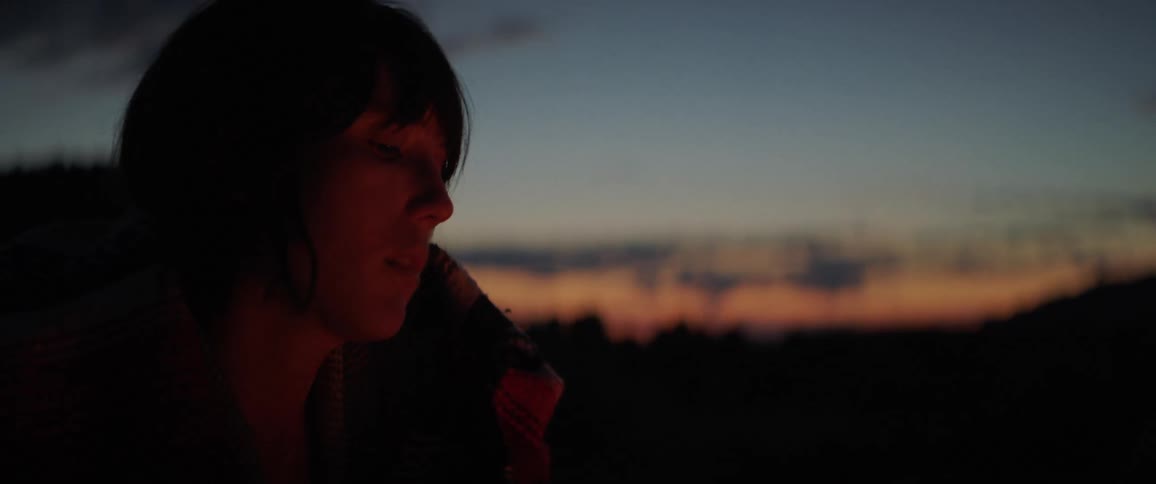 A sad looking woman sit in front of a camp fire