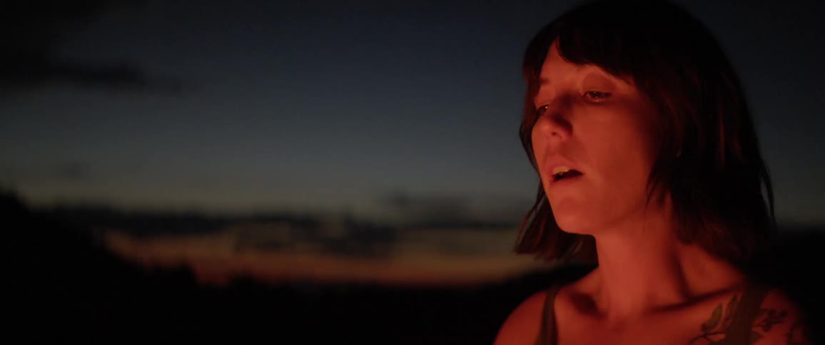 Woman standing next to the campfire breathe in deeply and then breathe out at dusk