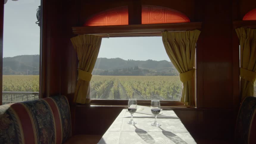 Two wine glasses on the table of a dining booth in the carriage of a moving train