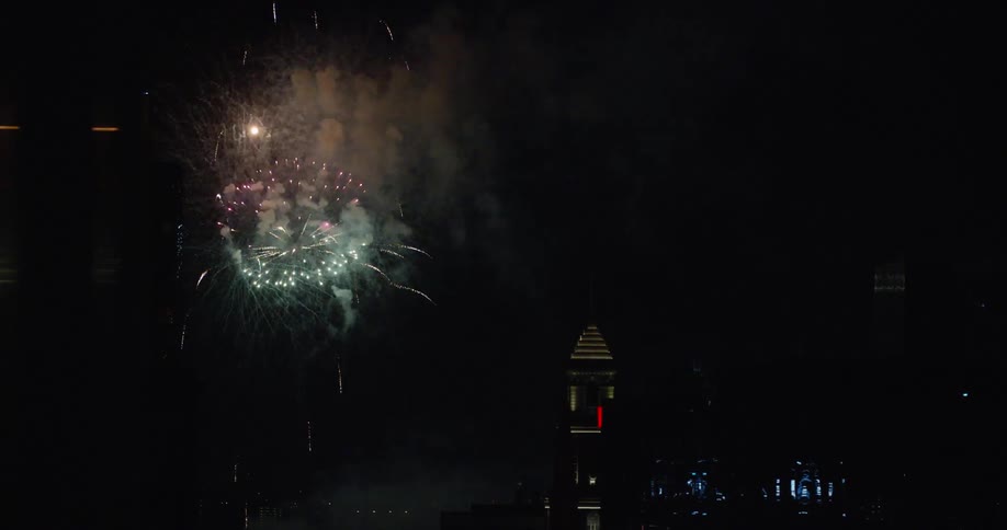 A number of fireworks explode in the nighttime sky above some tall buildings