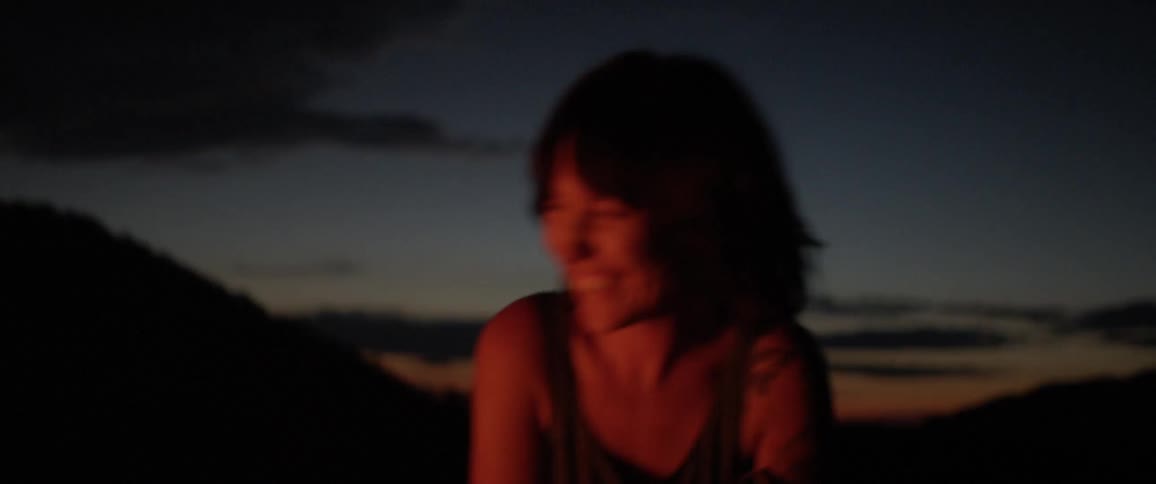 A woman with tattoos on her shoulder laughing by a fire at night