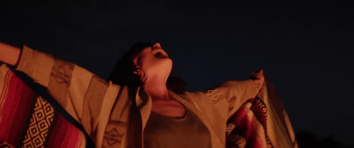 A young woman celebrate in front of a camp fire at the night