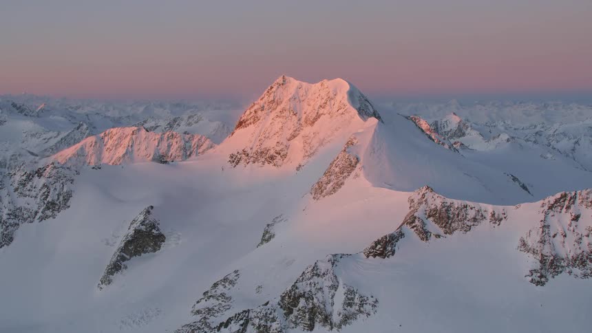 Aerial view of mountain range covered in snow at sunset
