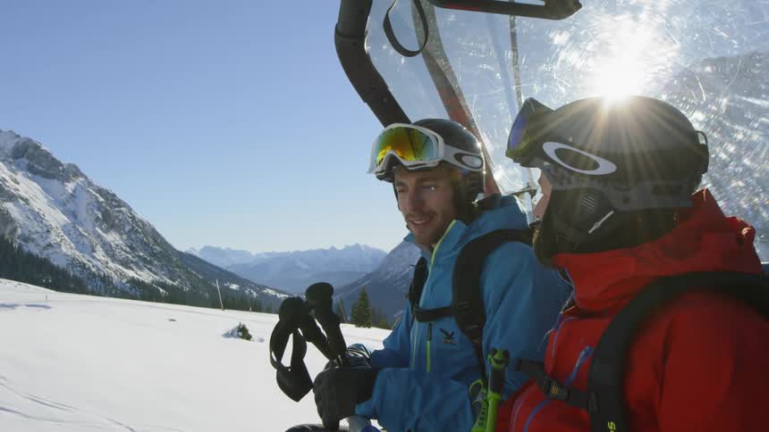 Two skierssmile and talk while on a ski lift on a sunny day