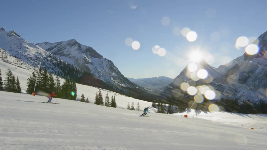 People ski down a mountain slope on a sunny day