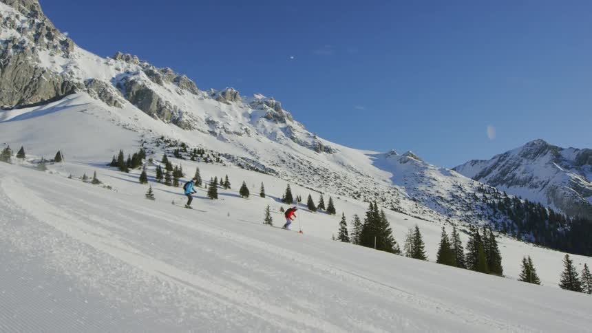 Skiers ski down the side of a snowy mountain under a blue sky