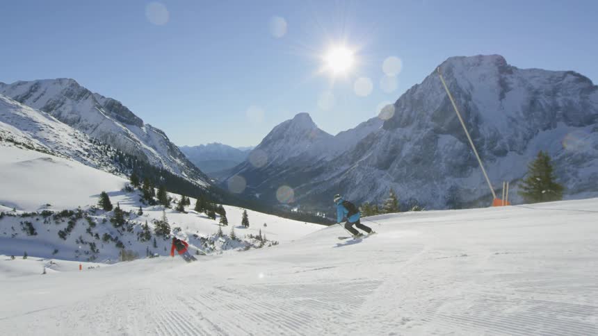 Two people wearing backpack ski down a slope