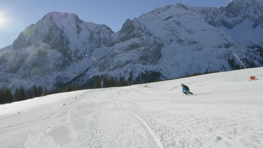 A person skis down a simple slope towards a large mountain