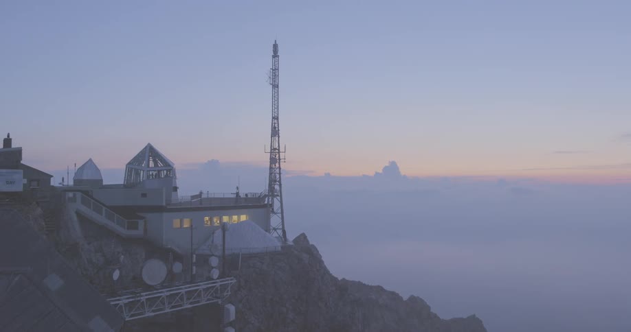 An building with an antenna and satellite dishes sits high up on a mountain