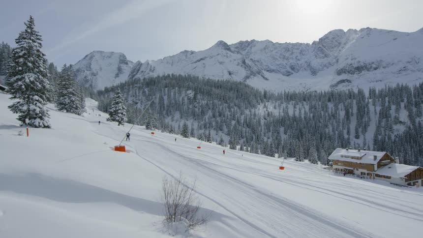 People ski down a mountain slope past a chalet