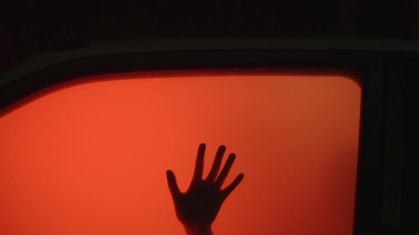 A car is lit up orange and a hand hits the window from the inside