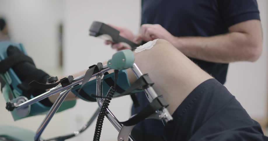 A physical therapist works on a patient with their knee and leg in a contraption