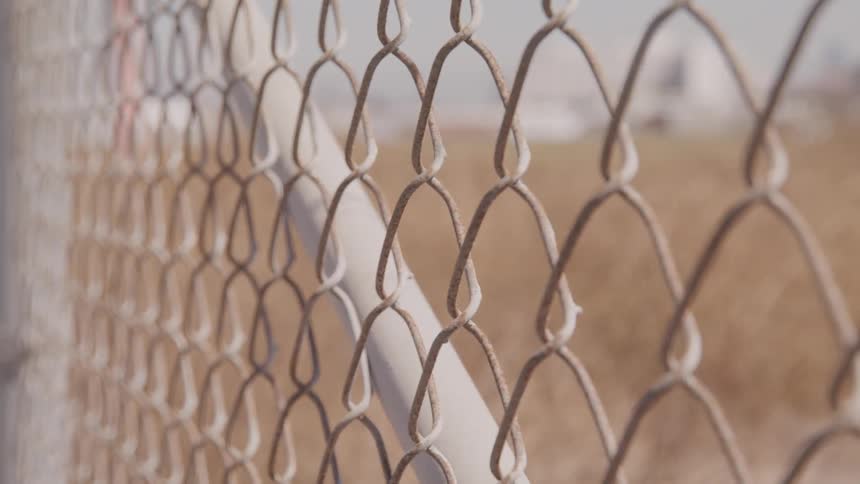 A brown field through a chain link fence on a sunny day