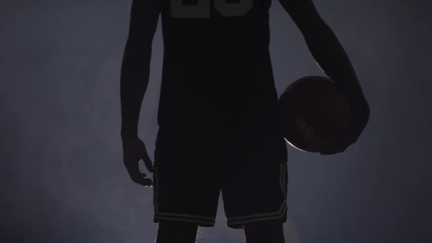 A man is holding a basketball in the dark