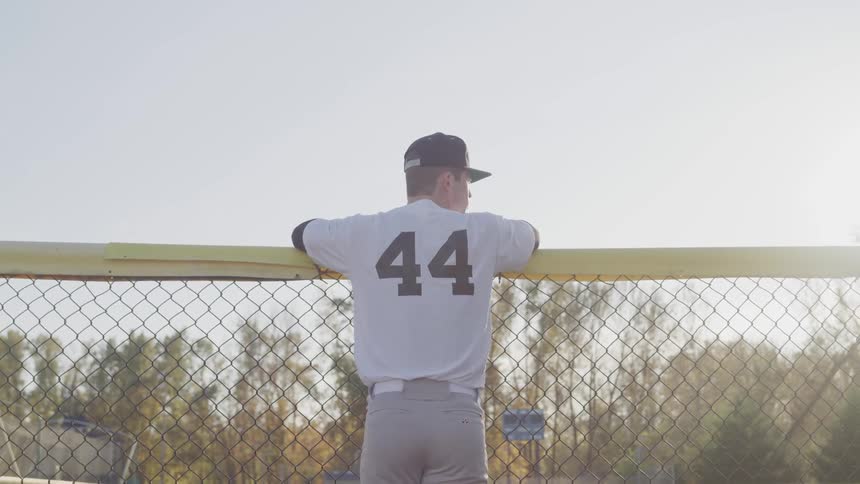 Man in baseball uniform leans against fence