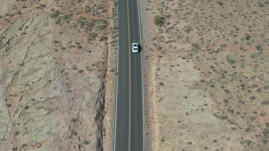 A car drives down a long flat road surrounded by desert