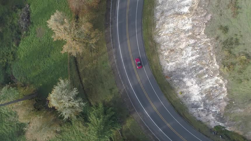 Red car drive along turn between fields and trees