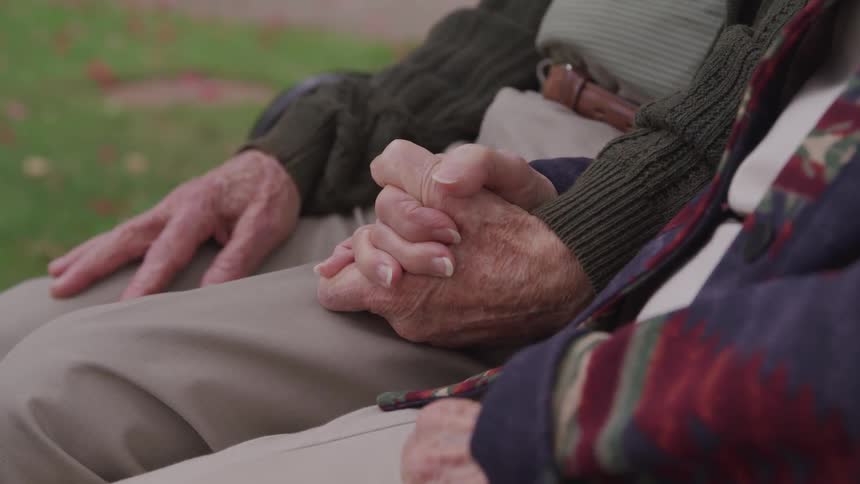 An elderly couple is holding hands while sitting outdoors