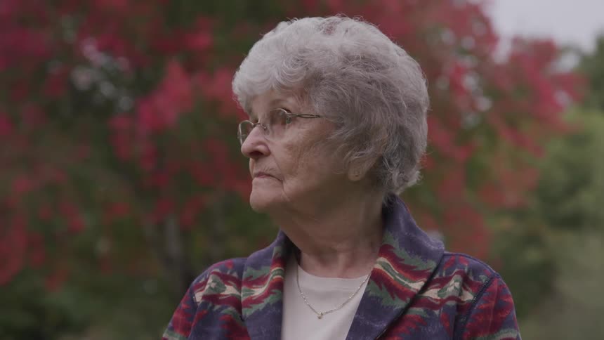 Senior old woman looks around in front of the red tree in the public park