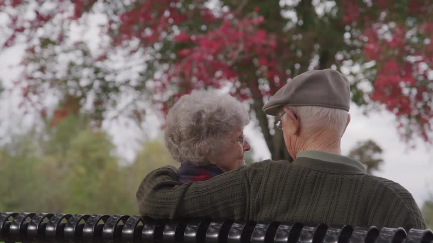 An elderly couple embracing while sitting on a bench in the park