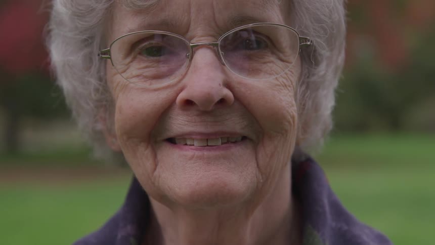 An elderly woman wearing glasses is smiling