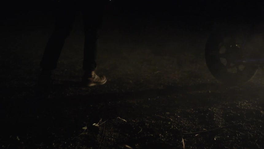 A man walks on a dirt path and up to a motorcycle