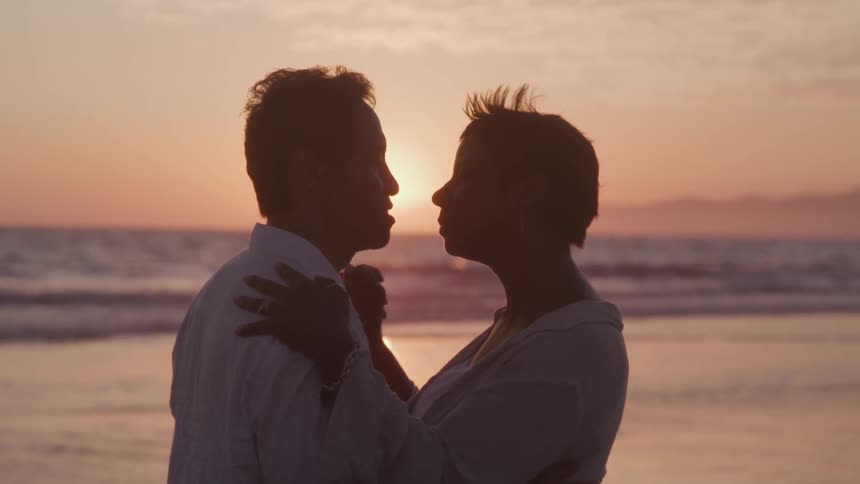 Man and woman dance and kiss on the beach at sunset