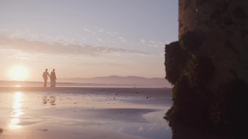 Man and woman walk along the beach at sunset next to the sea