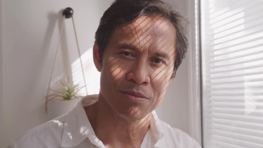 A man next to a window with a small plant behind him