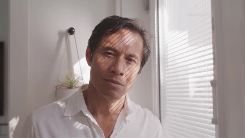 A man looks through blinds on a window and turns his head