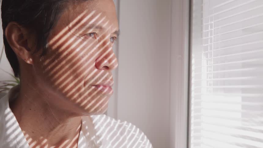 The man looks through the window blinds