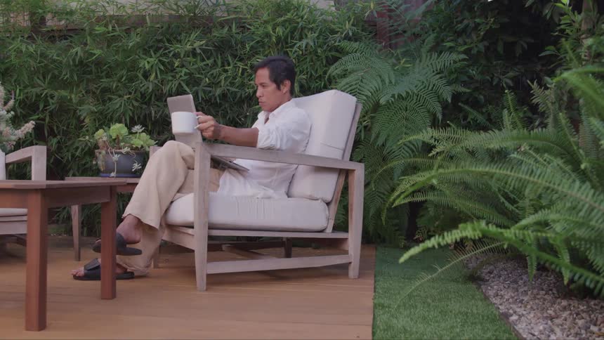A man relaxes on his patio with his laptop and a cup of coffee