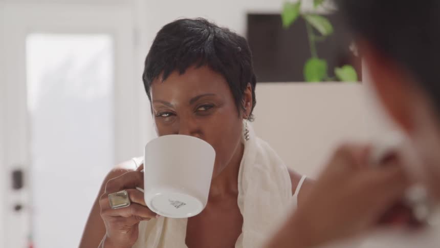 A woman takes a drink from a mug while sitting with another person