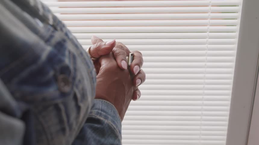 A woman in a denim jacket has her hands clasped together as if in prayer