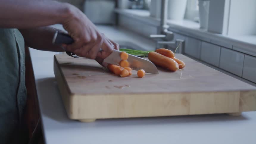 A person cuts a carrot on a wooden cutting board with a knife