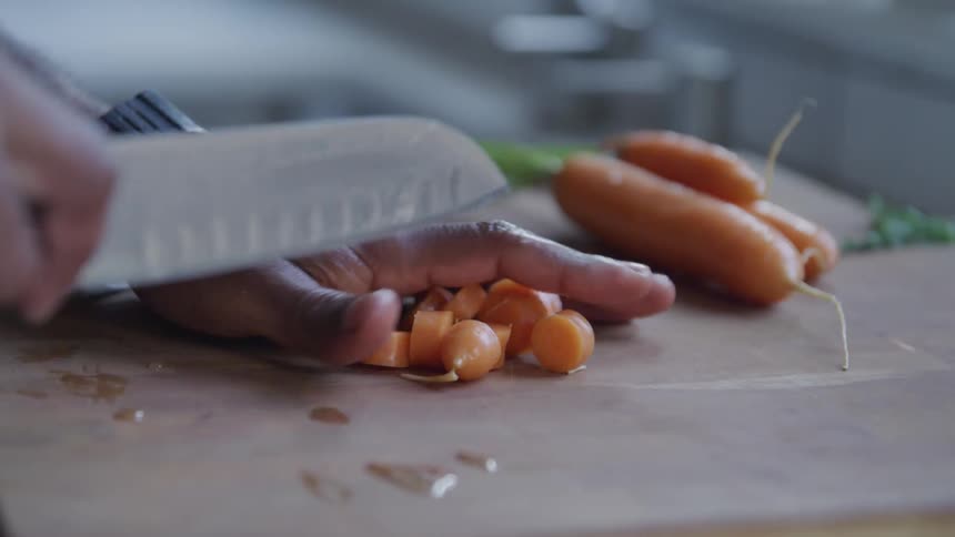 A person moves aside carrot slices on a cutting board as they prepare to cut up another one