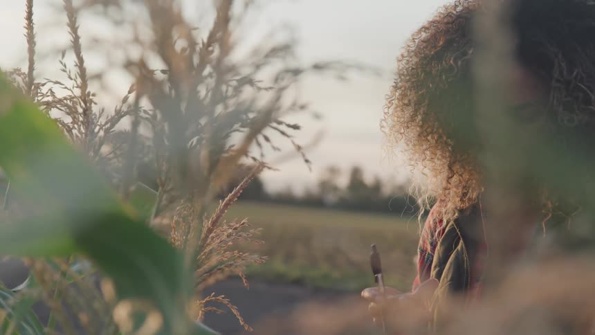 A woman is writing down notes while looking at some crops