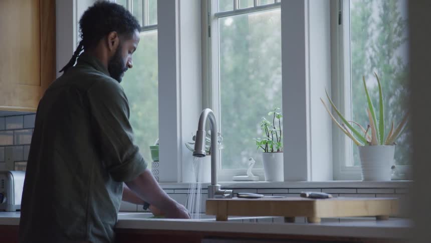 Man washes vegetables in the sink near window