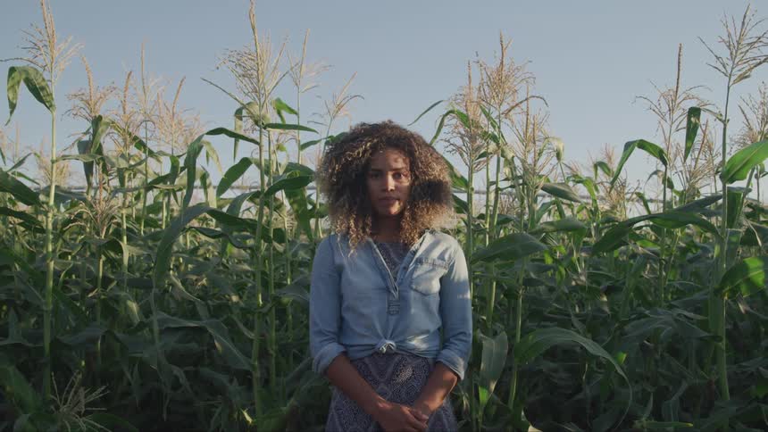 A woman stands with her hands clasped in a corn field