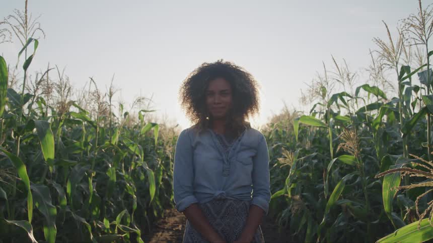A black woman turning her head to look at the camera while standing among tall crops