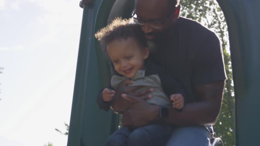 A grandfather holds his grandson as they ride down a slide