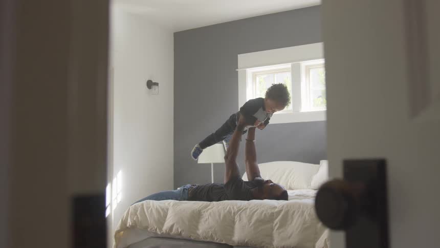 A man laying on a bed holding up a baby boy