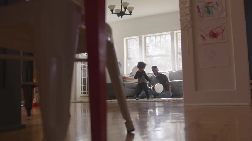 A dad is playing with a balloon with his son in their living room