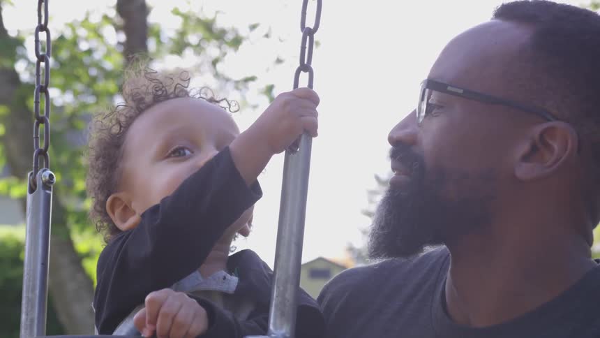 A man plays with a toddler in a swing